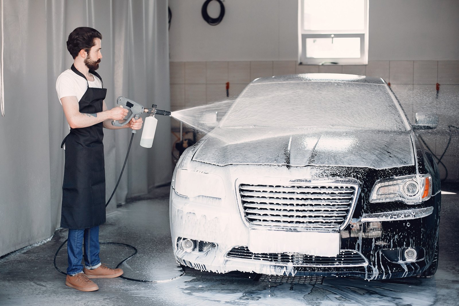 Man in a garage. Worker washing a car. Guy spray a soap